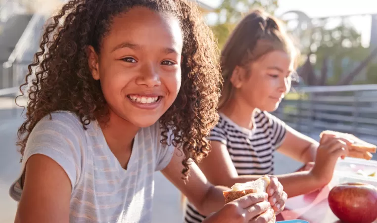 two happy girls eating lunch outside