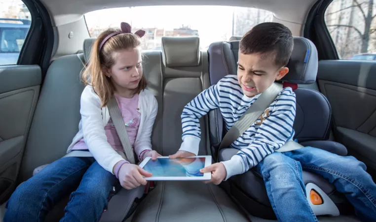 young brother and sister fighting over a tablet in the backseat of a car