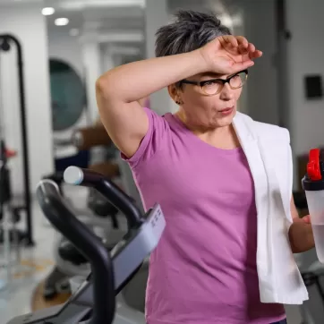 Mature tired woman wearing sportswear with bottle of water wiping her forehead